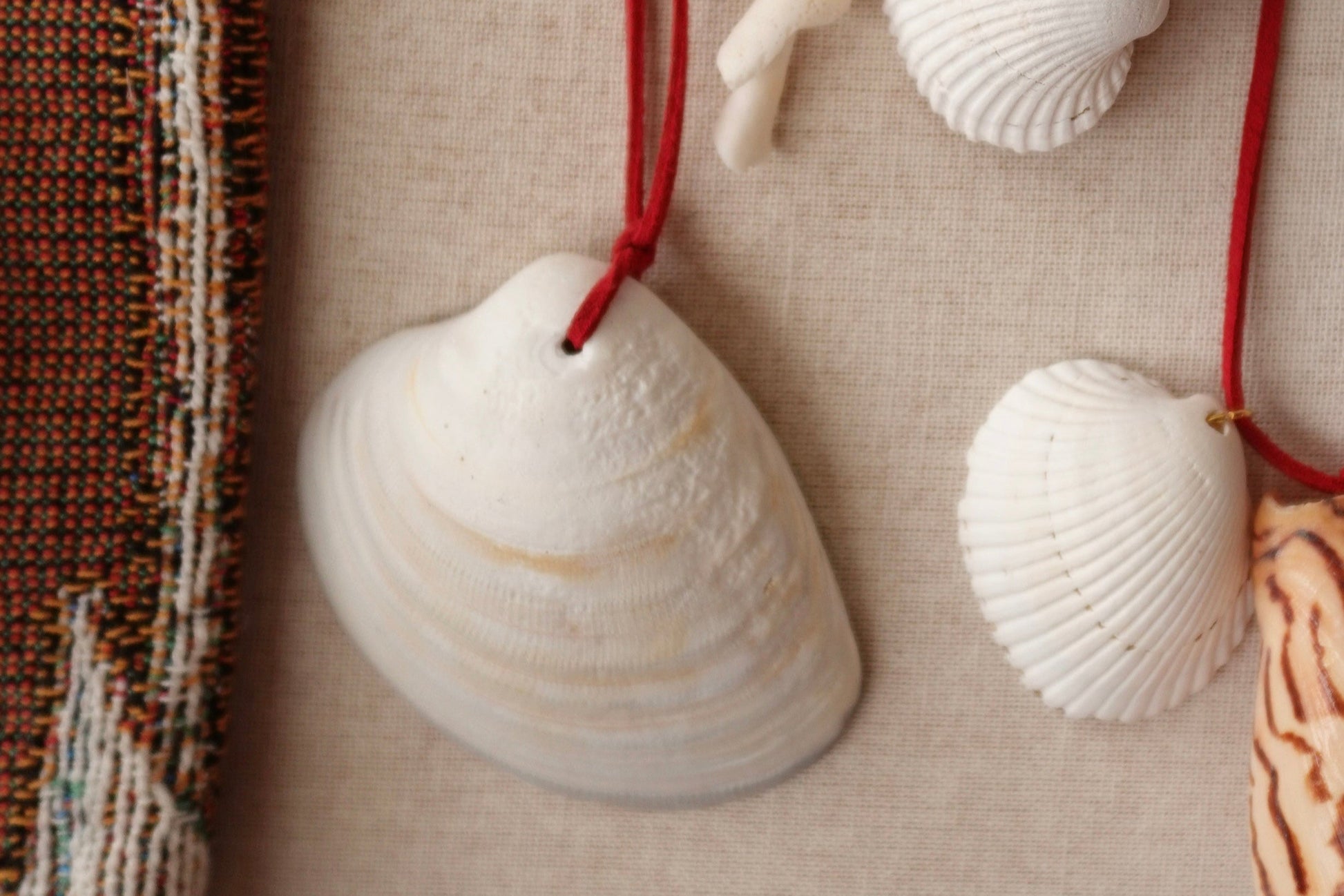 Seashell necklaces with red strings on a textured beige surface