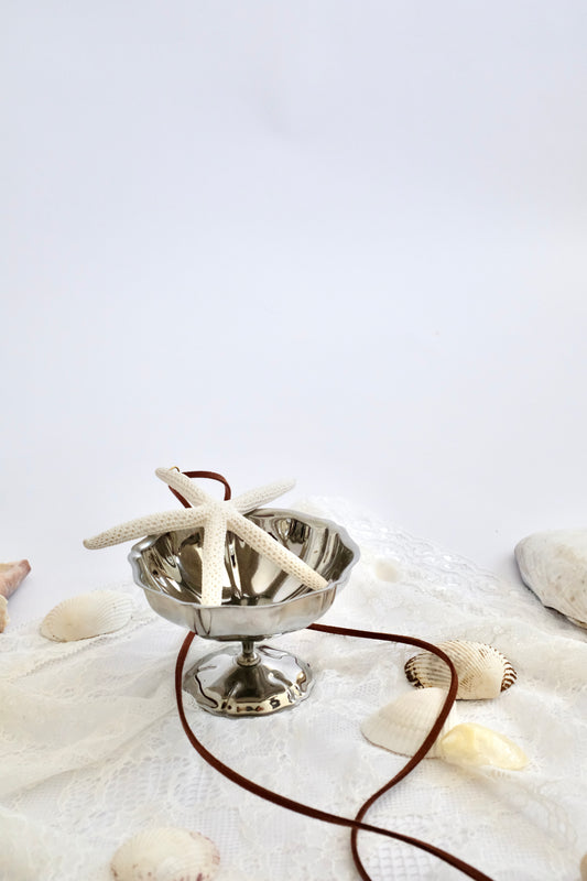 Silver bowl with starfish on a white surface with seashells