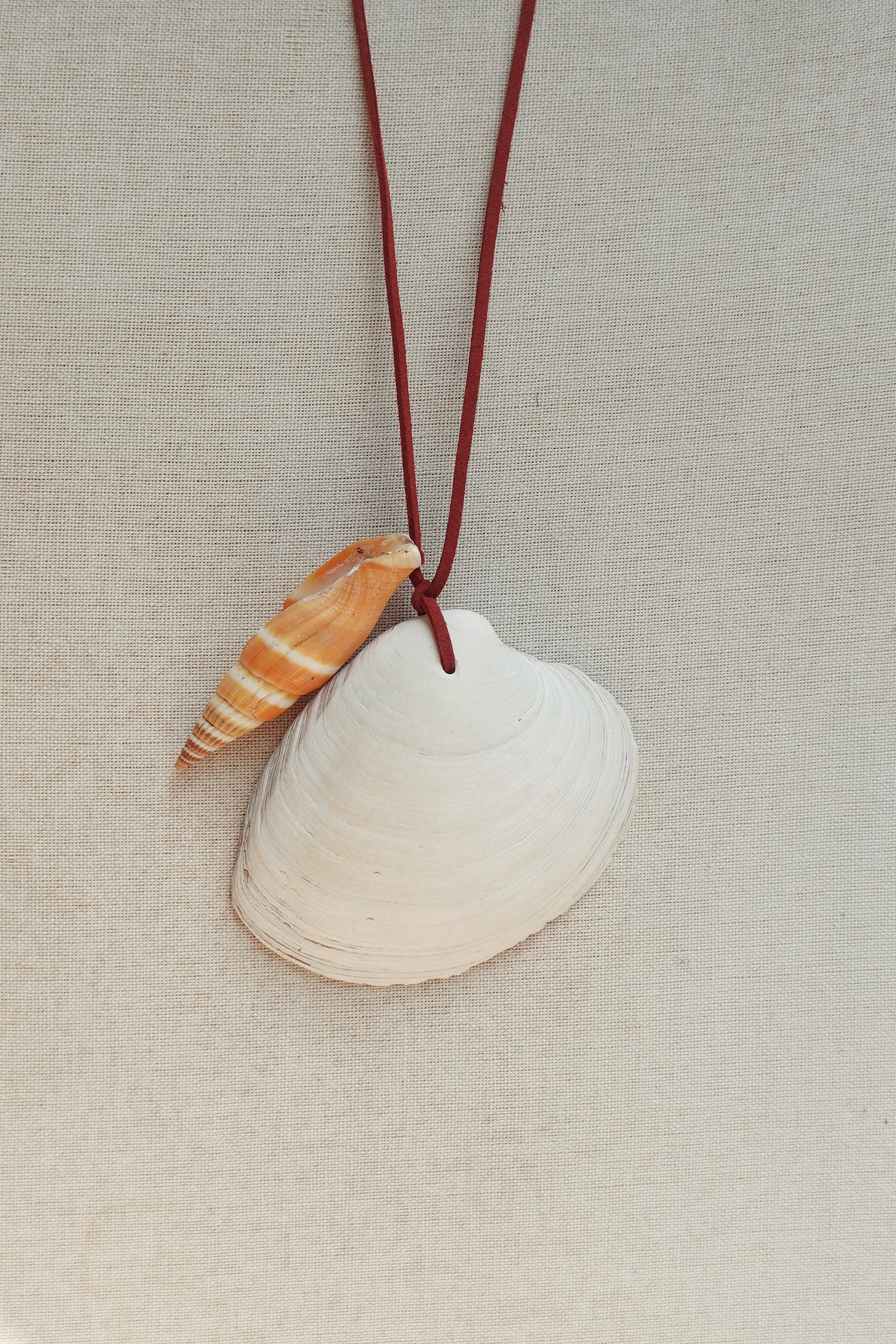 Necklace with a white shell and a small shell pendant on a beige fabric background